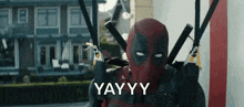 a man in a deadpool costume is holding a pair of swords in front of a house .