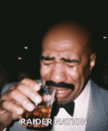 a man with a mustache drinking from a glass with the words raider nation written on the bottom