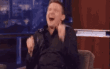 a man is sitting in front of a television with his arms in the air and laughing .