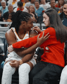 a woman in a red sweater is hugging a basketball player