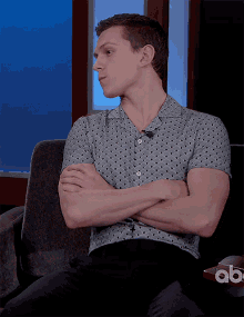 a man with his arms crossed is sitting on a couch in front of an abc sign