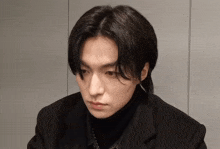 a young man with long black hair is wearing a black turtleneck and black jacket