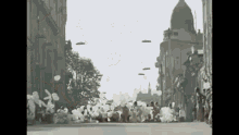 a black and white photo of a crowd of people walking down a street with balloons flying in the air .