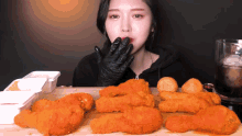 a woman wearing black gloves is eating fried chicken on a table