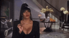 a woman in a black dress with a plunging neckline is smoking a cigarette in a living room .