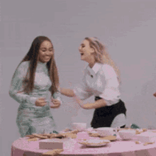 two women are laughing and hugging each other at a table with plates and bowls .
