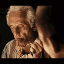an older man is eating spaghetti with a toothpick in his mouth