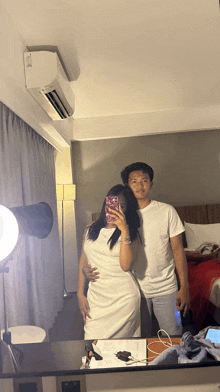 a man and a woman are taking a picture in front of a mirror