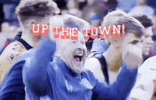 a man in a blue shirt is cheering with the words up the town behind him