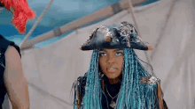 a girl with blue braids is wearing a pirate hat and making a funny face .