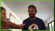 a man wearing a rams shirt is talking to another man in a room .