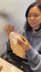 a woman in a blue hoodie is sitting at a table with her eyes closed holding a piece of paper .