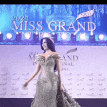a woman in a long dress is standing in front of a sign that says miss grand