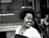 a black and white photo of a woman smiling while standing in front of a building .