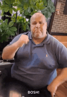 a fat man in a blue shirt is sitting at a table making a funny face .