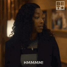 a woman with curly hair and a necklace is making a funny face and saying hmmm .