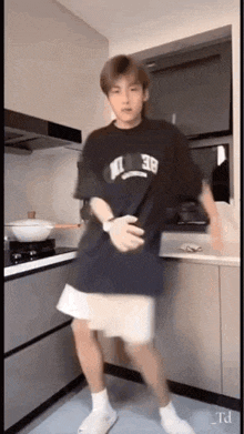 a young man is dancing in a kitchen with a pot on the stove .