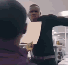 a man is holding a piece of paper in front of his face while another man looks on .