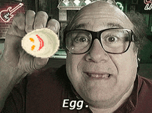 a man wearing glasses is holding up a pixelated egg with a smiley face on it and the words egg below him