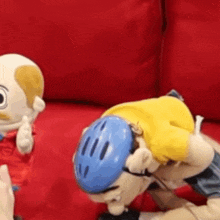 two stuffed animals are sitting on a red couch and one of them is wearing a helmet .
