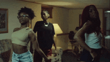 three women are dancing in a living room and one has red hair