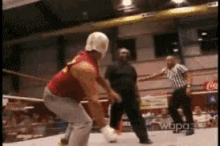 a man in a red shirt and white pants is standing in a wrestling ring with a referee
