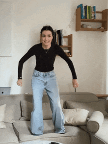 a woman in a black shirt and jeans is jumping on a couch in a living room
