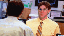 a man wearing glasses and a yellow shirt talks to another man