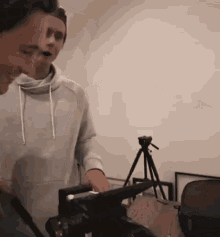 a man is holding a camera in a room with a tripod .