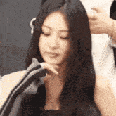 a woman with long black hair is looking at the camera with her hand on her chin .