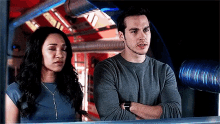 a man and a woman are standing next to each other with their arms crossed in a room .
