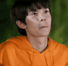 a young man wearing an orange hoodie is making a face .
