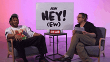a man and a woman are sitting in front of a sign that says hey ( ew )