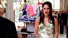 a woman in a green and white dress is standing in front of a rack of clothes and talking to another woman .