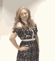 a woman in a black lace dress is standing with her hands on her hips and smiling .
