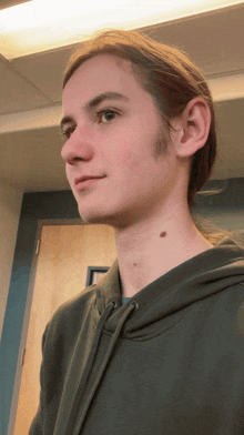 a young man with long hair is wearing a green sweatshirt