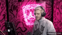 a man wearing headphones is standing in front of a microphone in front of a neon fist sign .
