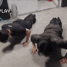 two men are doing push ups on the floor in front of a sign that says " play "
