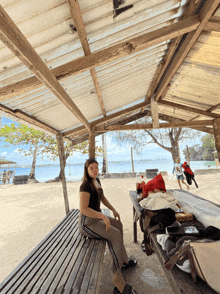 a woman sits on a bench under a roof overlooking the water