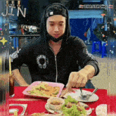 a person sitting at a table with a plate of food and a sign that says jin on it