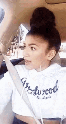 a woman is sitting in a car wearing a hollywood sweatshirt .