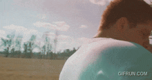 a gif from gifrun.com shows a man in a blue shirt standing in a field