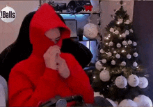 a man in a red hoodie is sitting in front of a christmas tree