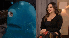 a woman is sitting next to a blue sculpture of a fish .
