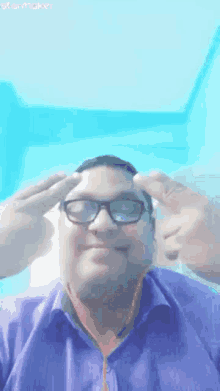 a man wearing glasses and a blue shirt is making a peace sign .