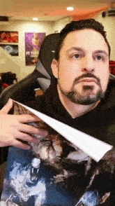 a man with a beard is holding a piece of paper with a picture of a wolf on it .