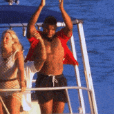 a shirtless man stands on a boat with his arms up in the air