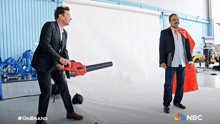 a man in a red cape is standing next to a man holding a blower
