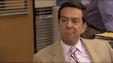 a man in a tan suit and pink tie is making a funny face