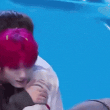 a man with pink hair is hugging another man with brown hair .